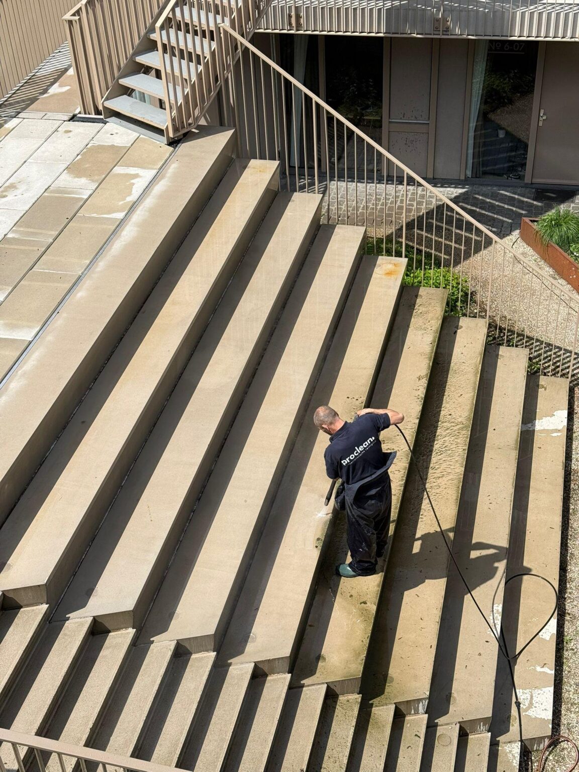 Medewerker van Proclean groep voert hogedrukreiniging uit op een buitentrap van een appartementencomplex.